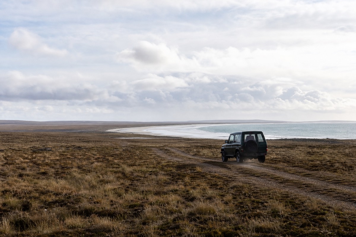A lone 4x4 crossing open treeless camp toward a distant white beach in the Falklands