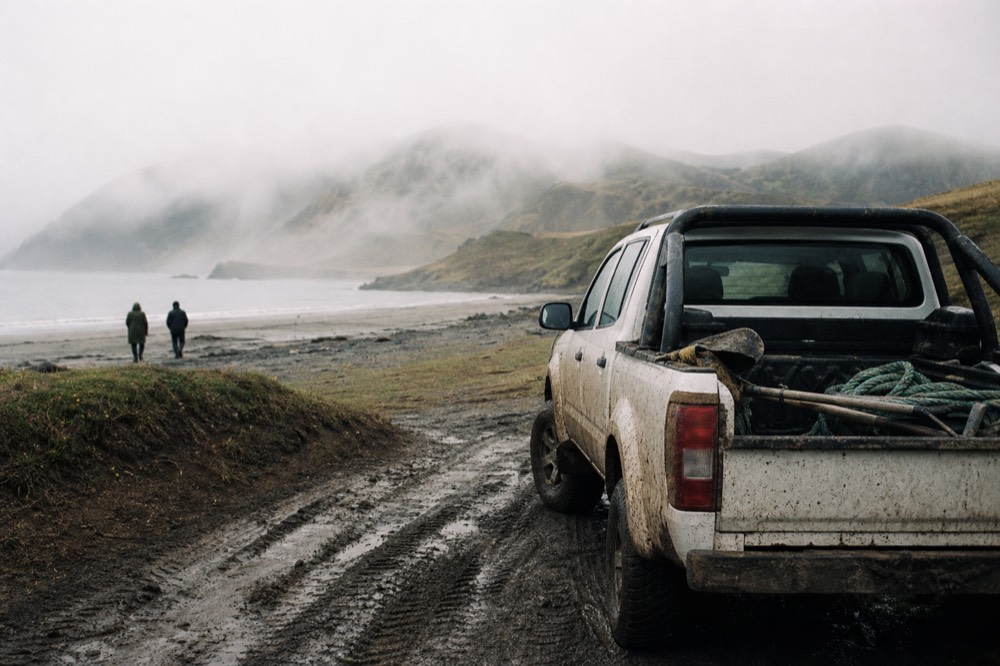 Mud-splashed four-wheel drive parked on a rutted track beside a peat bank, spades and a coil of rope in the open back, empty hills rolling away behind
