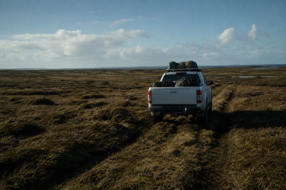 A white four-wheel-drive pickup crossing open moorland on a faint two-rut track, peat and grass running to a wide empty horizon