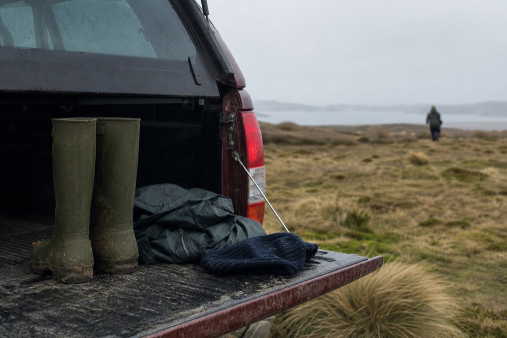 Waterproof boots, a folded wind shell and a woolly hat laid on a vehicle tailgate with brown moorland stretching behind