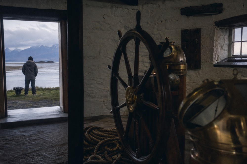 Interior of a small maritime museum with a wooden ships wheel, brass navigation instruments and coiled rope in a whitewashed stone room