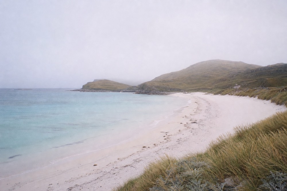 Empty white sand beach curving between low headlands with turquoise shallows, marram grass on the dunes and no footprints