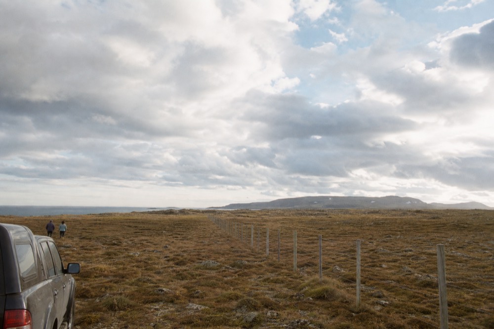 A wire fence running dead straight across brown moorland toward a distant low ridge, an enormous pale sky filling most of the frame